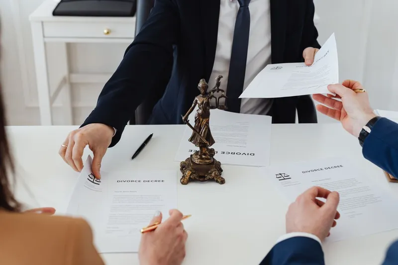 Two people at a table reviewing divorce papers with an attorney, a small Lady Justice statue between them